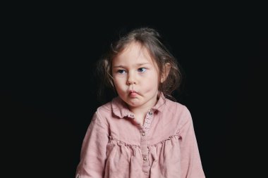 Stüdyoda siyah bir arkaplan karşısında etkileyici suratlar yapan hoş bir kız.