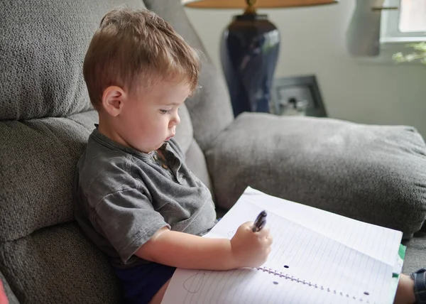 Młody Chłopiec Rysunek Bazgroły Notatniku Siedząc Kanapie Domu — Zdjęcie stockowe