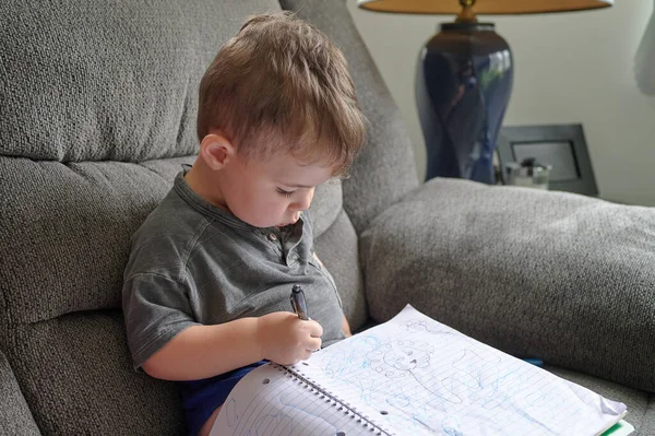 自宅のソファに座りながらノートに落書きをする少年 — ストック写真