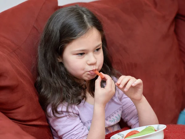 stock image expressive young girl is eating chicken and vegetables for dinner on the couch while watching TV