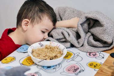 Yulaf ezmesinin soğumasını bekleyen genç bir çocuk.