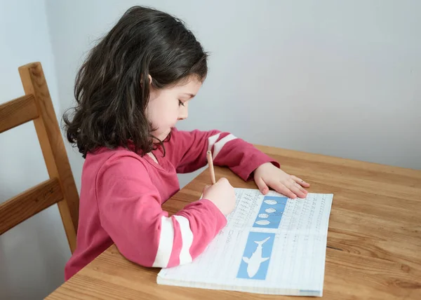 テーブルで文章を練習している少女が — ストック写真