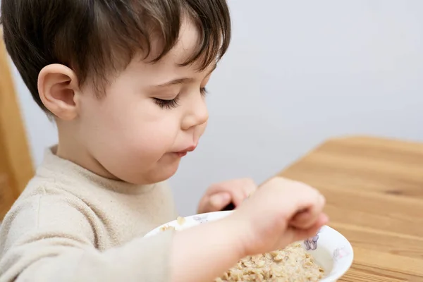 stock image little boy eating oatmeal for breakfast in the kitchen