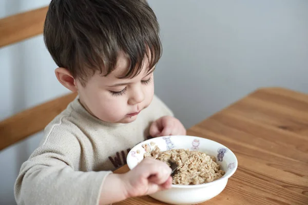 stock image little boy eating oatmeal for breakfast in the kitchen