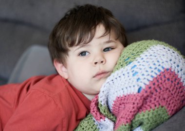 Kafası battaniyesinin içinde bir topun üzerinde kanepede dinlenen genç bir çocuğun portresi.