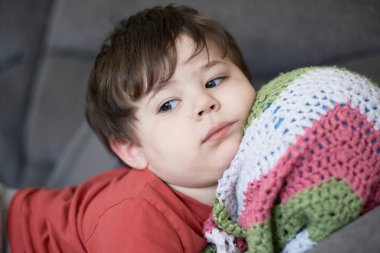 Kafası battaniyesinin içinde bir topun üzerinde kanepede dinlenen genç bir çocuğun portresi.