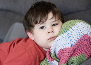 Kafası battaniyesinin içinde bir topun üzerinde kanepede dinlenen genç bir çocuğun portresi.