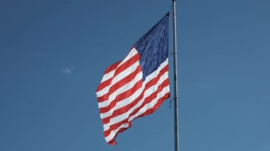 Birleşik Devletler bayrağı yavaş çekimde sallanıyor açık mavi gökyüzüne karşı birkaç ince bulutlu 
