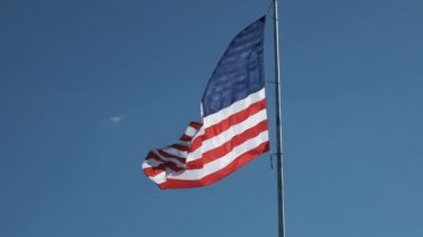 Birleşik Devletler bayrağı yavaş çekimde sallanıyor açık mavi gökyüzüne karşı birkaç ince bulutlu 