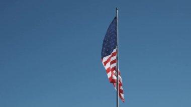 Birleşik Devletler bayrağı yavaş çekimde sallanıyor açık mavi gökyüzüne karşı birkaç ince bulutlu 