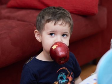 Oturma odasında elma yiyen tatlı çocuk.