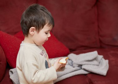 Oturma odasında bir dilim peynir yiyen tatlı çocuk.