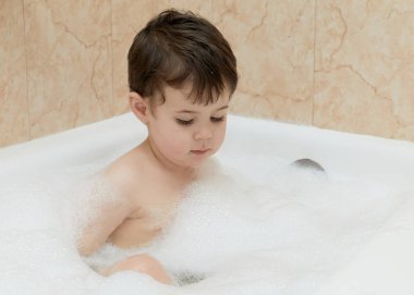 Tatlı çocuk küvette köpüklerle oynuyor.