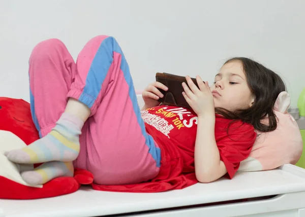Genç kız odasında uzanırken cep telefonuyla oynuyor.