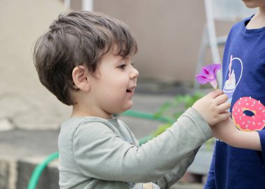 Kardeşler arka bahçede mor bir çiçekle oynuyorlar.