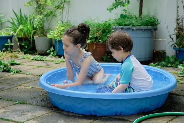 Brother and sister playing in a shallow pool in the backyard