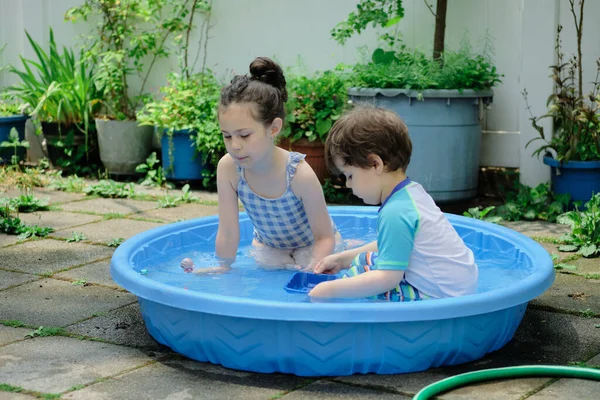 Brother and sister playing in a shallow pool in the backyard
