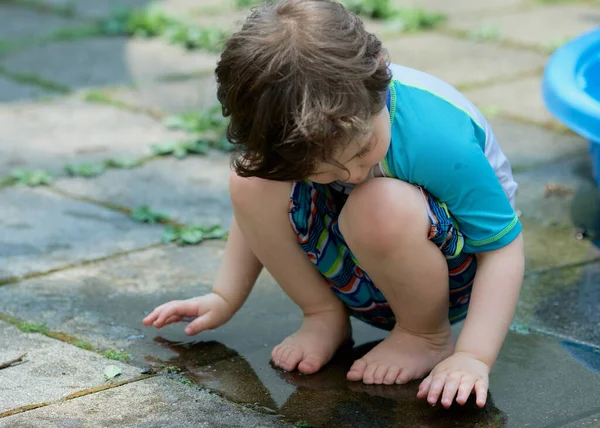 stock image young boy in a bathing suit playing in a puddle of water in the backyard