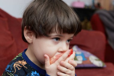 Etkileyici genç çocuk oturma odasındaki Noel ağacının önünde domates yiyor.