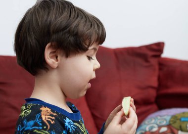 Dinazor pijamalarıyla kanepede salatalık yiyen tatlı bir oğlan.