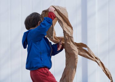 Küçük çocuk arka bahçede kahverengi ambalaj kağıdıyla oynuyor.