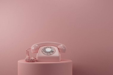 Pembe bir kaidede, pembe bir duvarın üzerinde oturan pembe bir telefon.