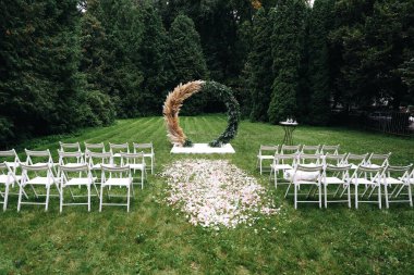 Düğün kemeri dışarıda kumaş ve çiçeklerle süslenmiş. Güzel bir düğün hazırlığı. Bahçedeki yeşil çimlerde düğün töreni. Dekorasyonun bir parçası, çiçek aranjmanı. Yüksek kalite fotoğraf