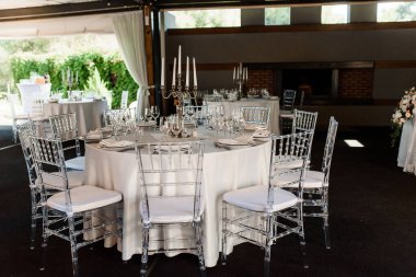 Büyük, uzun, süslü, ahşap bir masa ve tabakla kaplı beyaz bir masa örtüsü.