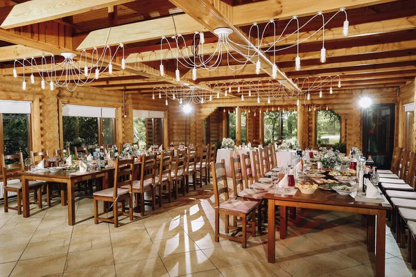 Banquet wooden hall for a rustic wedding with round decorated tables, Viennese chairs with flowered leaves and tablecloths. Horizontal. High quality photo