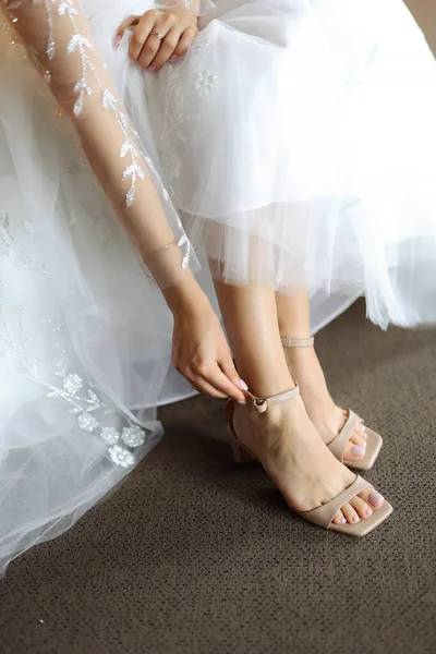 Bride\'s morning. The bride is putting her shoes on Close up of bride\'s legs in beautiful shoes. Preparing for the wedding. Bride wearing white wedding dress and shoes. white shoes on the feet .