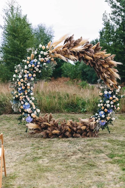 Luxurious yellow-gold wedding arch decorated with white flowers in nature among the trees. wedding ceremony. white piano on the nature. chairs for guests on the street. High quality photo