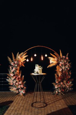 Bir düğün arkaplanının önünde duran beyaz bir pasta ve Edison lambaları açık, kemerde bir akşam düğünü, düğün davetlileri için bir pasta, bir doğum günü pastası. Yüksek kalite fotoğraf