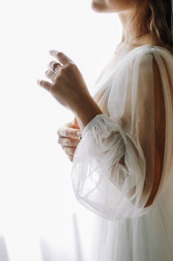 Gelin, pencerede duruyor, dantel kolunu ayarlıyor. Yüksek kalite fotoğraf