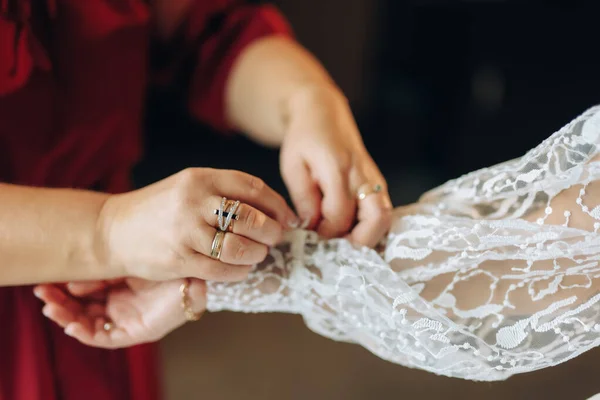 彼女は花嫁が袖をボタンでウェディングドレスを着るのを助けます 高品質の写真 — ストック写真
