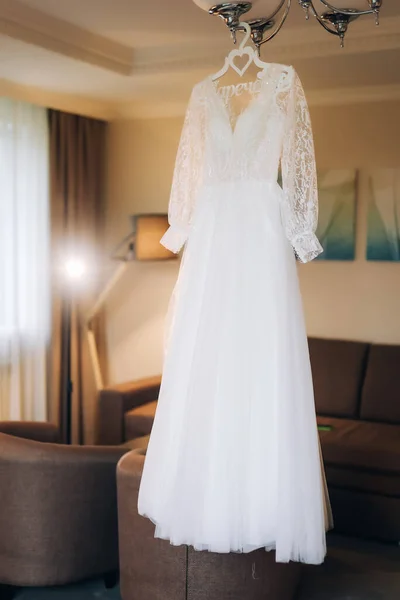 The perfect wedding dress with a full skirt on a hanger in the room of the bride with blue curtains. High quality photo