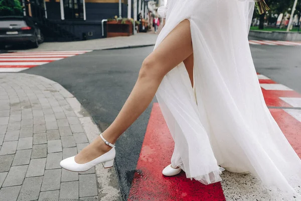 新娘的腿穿着时髦的凉鞋 水晶与高跟鞋从婚纱下窥探出来 高质量的照片 — 图库照片