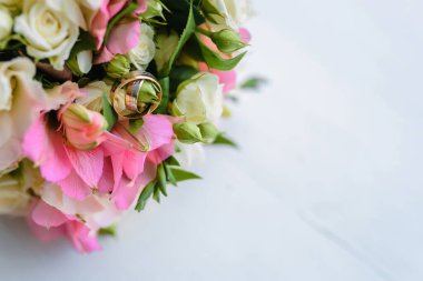 Evlilik yüzükleri, gelin aksesuarı olarak güzel bir buketin üzerinde bulunur. Altın alyansların yakın plan görüntüsü ve ahşap masa üstünde güzel mavi çiçekler. Yüksek kalite fotoğraf