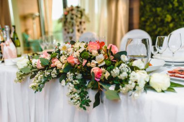 Beyaz bezle kaplı uzun yemek masaları porselen ve mavi bardaklarla servis edilmiş ve bir evin çatısında çiçeklerle süslenmiş. Yüksek kalite fotoğraf