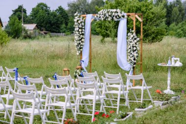 Bir parkın açık hava düğünü. Düğün kemeri sahada, chiavari sandalyeler sergileniyor. Yüksek kalite fotoğraf