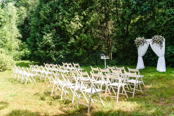 Wedding arch decorated with cloth and flowers outdoors. Beautiful wedding set up. Wedding ceremony on green lawn in the garden. Part of the festive decor, floral arrangement. High quality photo