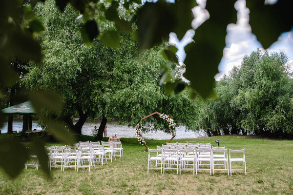 A beautiful venue for an open-air wedding ceremony. Wedding arch and rows of guest chairs on a green lawn overlooking the river. High quality photo