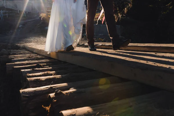 在日落时走在木桥上的新婚夫妇 高质量的照片 — 图库照片