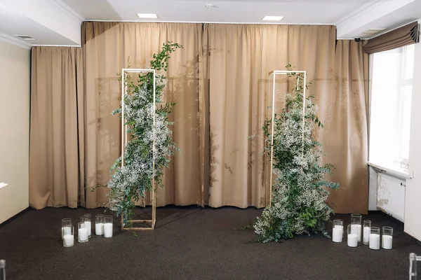 Indoor wedding ceremony with white wedding arch decorated with flowers and big white candles. High quality photo. High quality photo. High quality photo