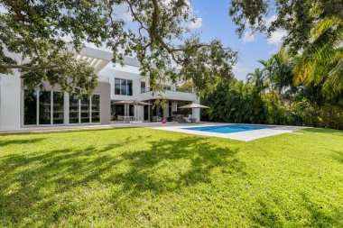 Miami 'de havuzlu, kısa çimenli, ağaçlı, palmiye duvarlı, şemsiyeli, balkonlu, sandalyeli ve masalı, yaz mutfağı olan güzel, zarif ve modern bir evin arka bahçesi.
