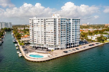 Arka planda modern binalar, mavi gökyüzü, mavi okyanus, yüzme havuzları, palmiye ağaçları olan Miami sahillerinin insansız hava aracı görüntüsü.