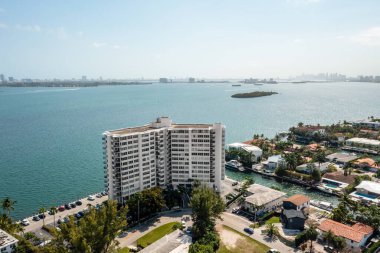 Arka planda modern binalar, mavi gökyüzü, mavi okyanus, yüzme havuzları, palmiye ağaçları olan Miami sahillerinin insansız hava aracı görüntüsü.