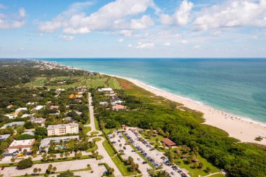 Büyük tropikal bitki örtüsü, kuleler ve modern binalar ve arka planda deniz olan bir Miami mahallesinin insansız hava aracı görüntüsü..