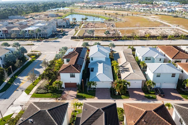Aerial drone shot residential neighborhood, with several houses under construction, boulevard with trees, lagoon with fountain, urban skyline, blue sky in the background