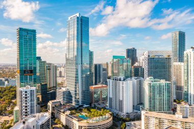 Modern Miami binaları, gökdelenler, tropikal bitkilerle dolu havuz alanları, mavi gökyüzü.