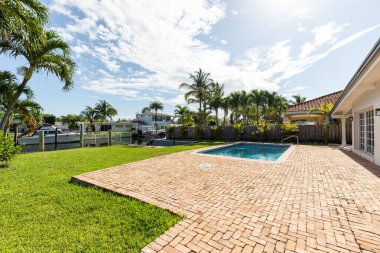 Havuzlu veranda, ahşap parti duvarı, tropikal bitkiler, rıhtım, yatlar ve mavi gökyüzü.